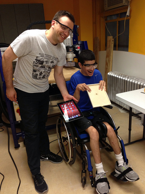 two people standing in front of a CNC machine holding a wooden ipad holder